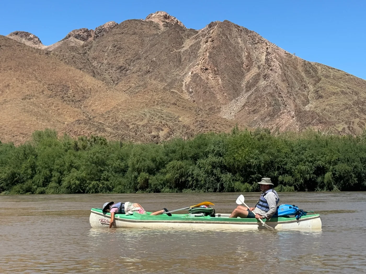 An adult paddling an open canoe while a child rests at the front