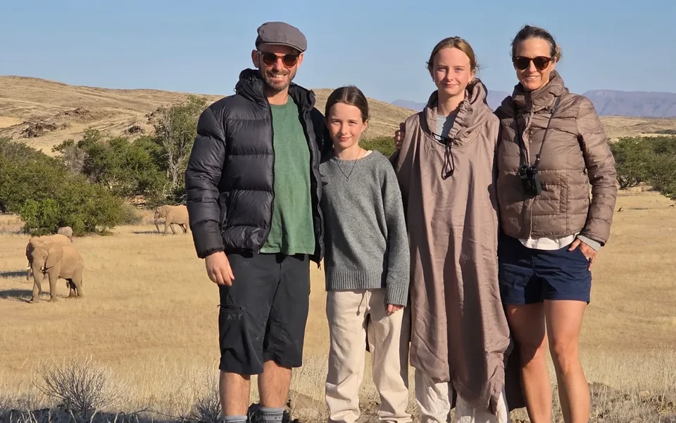 The Sparks family standing together on a rocky plain with elephants grazing behind them in Namibia