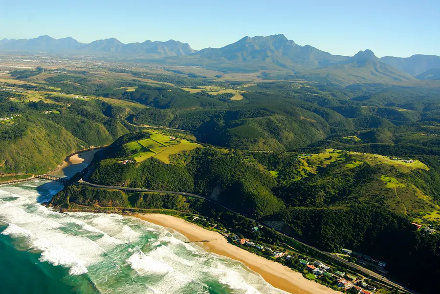 Aerial view of the Garden Route coastline with surf, sandy beach and forested mountains near Wilderness, South Africa