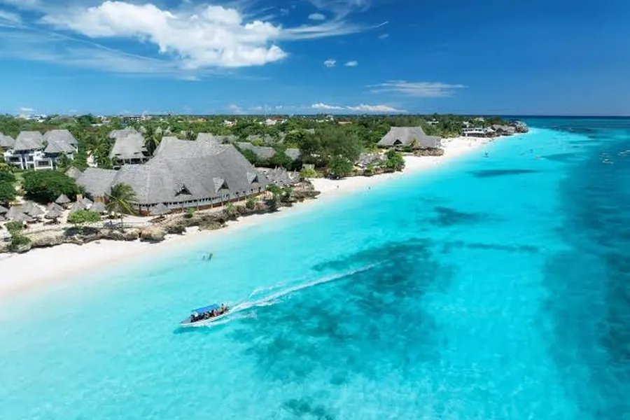 Aerial view of a thatched Zanzibar beach resort on white sand beside turquoise Indian Ocean shallows