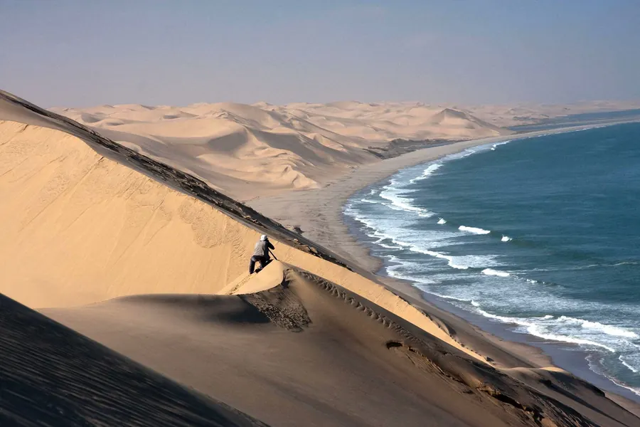 Walker on a giant sand dune where the Namib Desert meets the Atlantic surf on the Skeleton Coast, Namibia