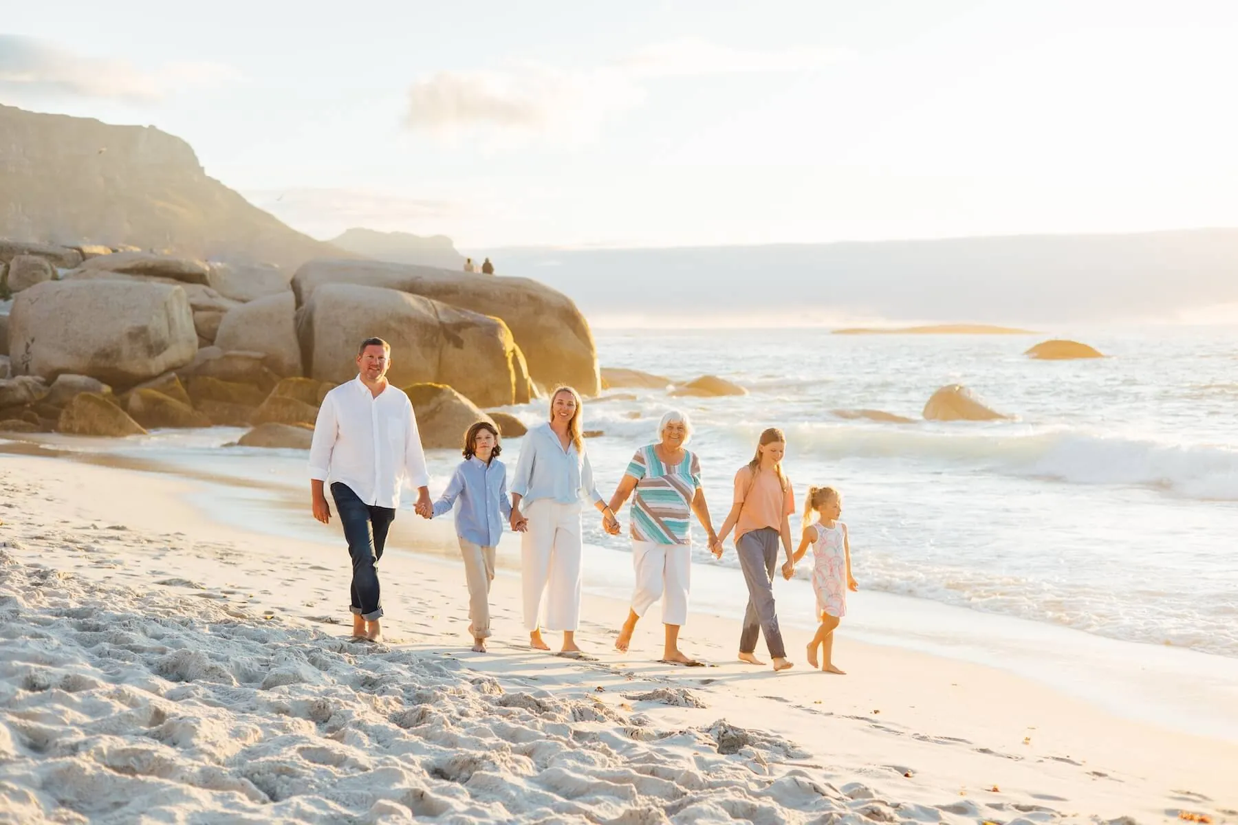 Three generations of a family walking hand-in-hand along a Cape Town beach at golden hour